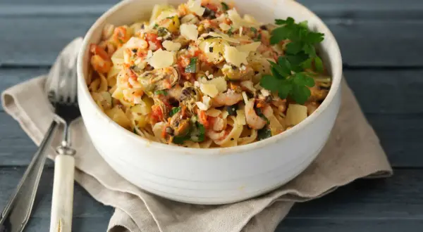 En skål med frutti di mare pasta, toppad med parmesan och persilja, serverad med en gaffel på en duk.