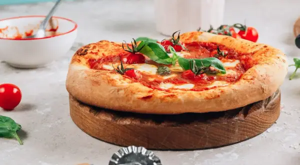 Pyszna pizza na drewnianej desce, gotowa do pokrojenia. Idealna do piekarnika, dzięki kamieniowi do pizzy.