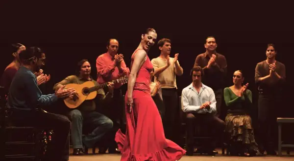 Una vibrante artista flamenco, con un vestido rojo, baila apasionadamente mientras músicos la acompañan.