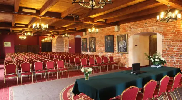 Elegancka sala konferencyjna w hotelu z **luxury collection**, z rzędami czerwonych krzeseł, drewnianym sufitem i ceglanymi ścianami.