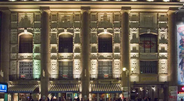 Der Admiralspalast Berlin bei Nacht, beleuchtet mit Säulen und Verzierungen. Menschen stehen vor den Eingängen und Cafés.