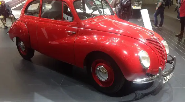En glänsande röd ifa bil står på ett mörkt golv. Bilen har en rundad form och kromade detaljer.