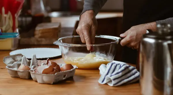 Préparation d'une crème pâtissière façon Cyril Lignac : des œufs battus dans un bol, des coquilles d'œufs à côté.