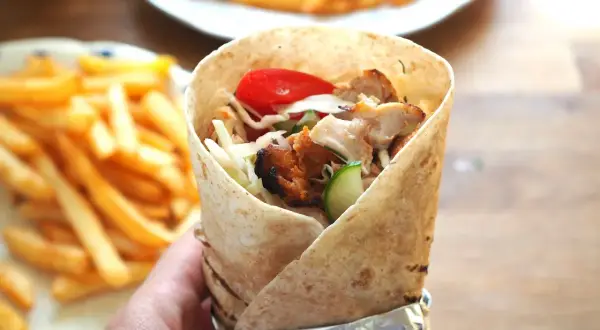 Pyszny kebab amerykański z kurczakiem, warzywami i frytkami na talerzu.