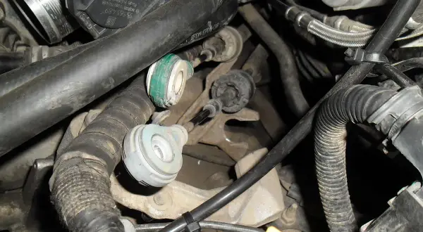 Widok na mechanizm skrzyni biegów z widocznymi linkami zmiany biegów, przewodami i elementami silnika.