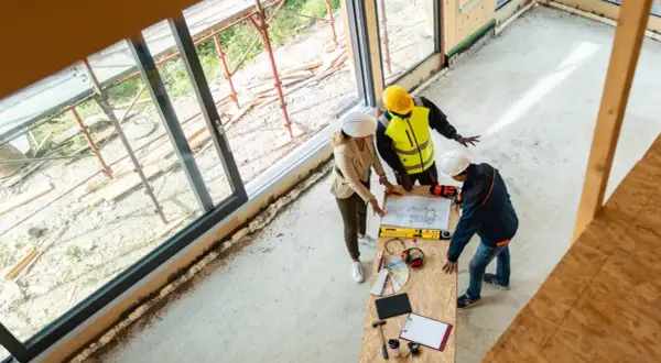 Architekci omawiają projekt, ustalając, ile kosztuje strop drewniany. Na stole plany, narzędzia i próbki materiałów.