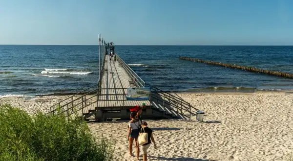 Sianożęty atrakcje: drewniane molo na plaży, ludzie spacerują, morze i niebo.