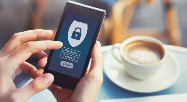 Dłoń trzyma smartfon z ekranem logowania do bankowości internetowej. Widoczne pole na hasło i ikonka kłódki symbolizują bezpieczeństwo.