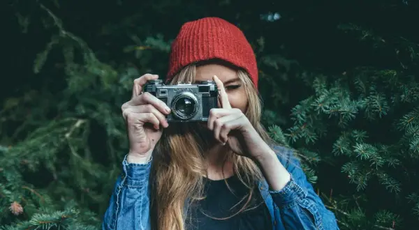 Dziewczyna w czerwonej czapce i dżinsowej kurtce trzyma aparat, gotowa do uchwycenia piękna przyrody. To jej dzień fotografa.