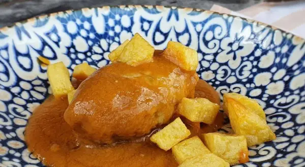 Rollo de bonito asturiano bañado en salsa, acompañado de patatas fritas en dados, servido en un plato azul y blanco.