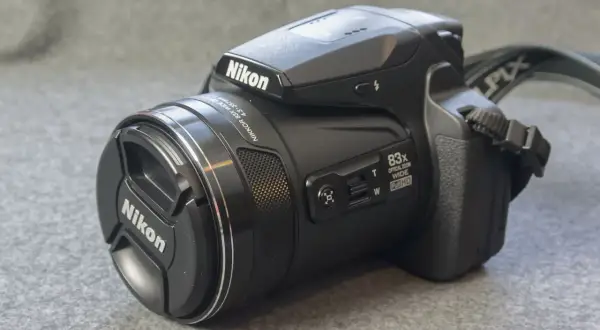 A black Nikon P90 camera with an 83x optical zoom lens sits on a textured gray surface.