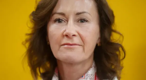 Helena Hedblom, en kvinna med brunt hår och en varm blick, poserar framför en solgul bakgrund.