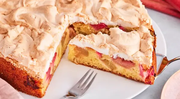 Saftiger Rhabarberkuchen mit luftigem Baiser, ein Stück ist schon angeschnitten.