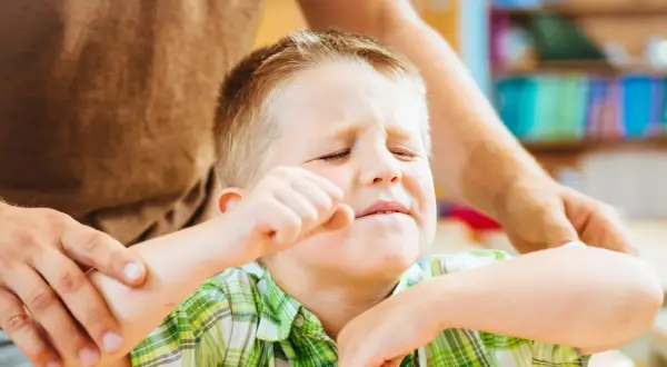 Chłopiec zamyka oczy, zaciska pięść, a dorosły trzyma go za ramię. Szukamy odpowiedzi, jak leczyć ADHD, by pomóc dzieciom.
