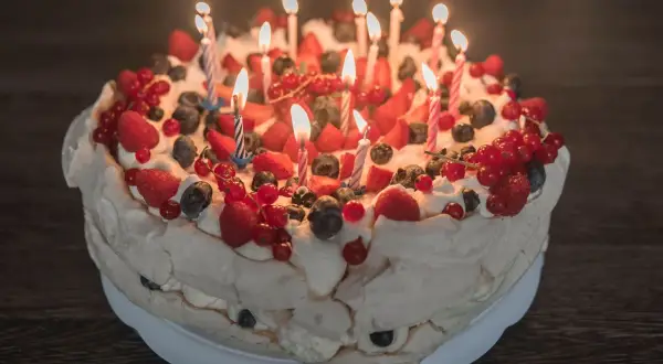 Pyszne ciasto urodzinowe z bitą śmietaną, truskawkami, malinami, borówkami i porzeczkami, ozdobione płonącymi świeczkami.