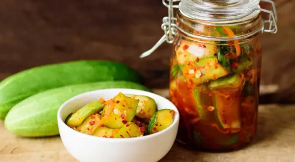 Słoik i miseczka z pikantnymi ogórkami z papryką chili, obok świeże ogórki.