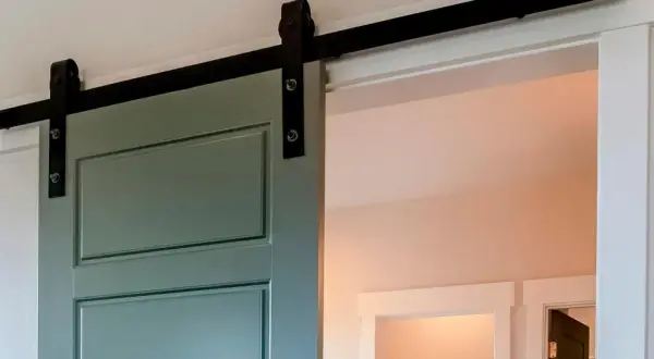 Trasformare porta battente in scorrevole: una porta verde con sistema a vista su binario nero, soluzione moderna per ottimizzare gli spazi.