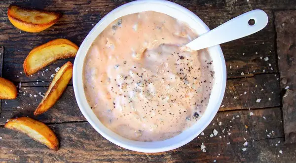 En skål med krämig hamburgerdressing, perfekt för ditt nästa hamburgerdressing recept. Serveras med klyftpotatis på en träbakgrund.
