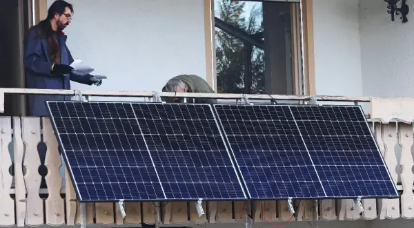 Dos hombres instalan placas solares en una terraza. Uno revisa un papel mientras el otro se inclina sobre los paneles.