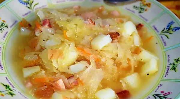 Gęsty, sycący kapuśniak z ziemniakami i kawałkami wędzonki, podany w ozdobnej misce.