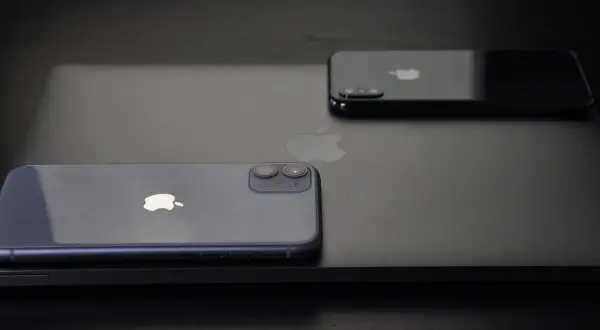 Dwa iPhone'y, w tym jeden fioletowy, leżą na czarnym laptopie. Zastanawiasz się, jak wyłączyć iPhone'a 11?