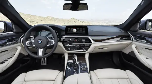 Wnętrze g30 bmw z jasną tapicerką, kierownicą i ekranem multimedialnym. Widok na pustynny krajobraz przez przednią szybę.