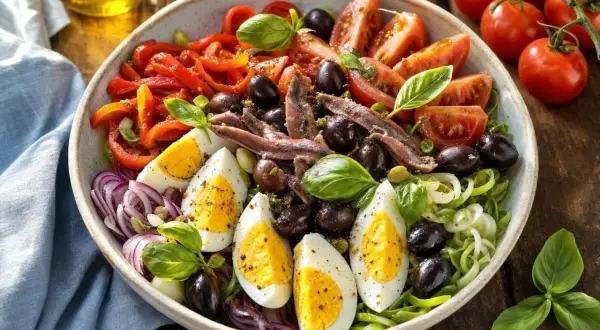 Salade de riz niçoise colorée avec œufs durs, tomates, poivrons, olives, anchois et basilic frais. Un délice méditerranéen.