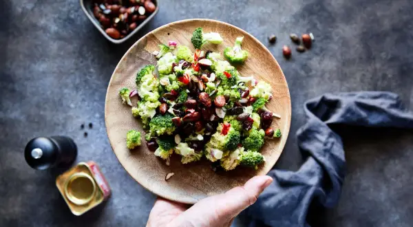 Frischer Brokkoli Salat mit Nüssen und roten Zwiebeln auf einem Holzteller, bereit zum Genießen.