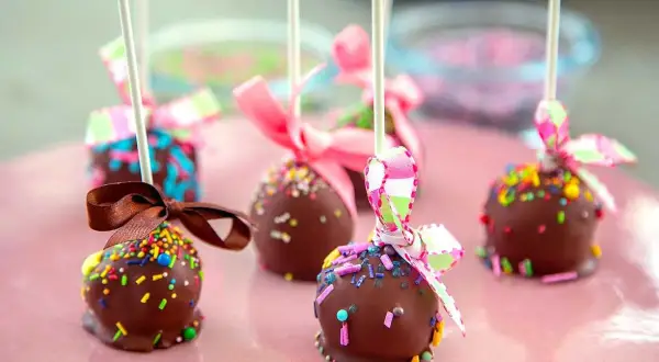 Chokladöverdragna cake pops med färgglada strössel och fina band. Perfekta för ett kalas!