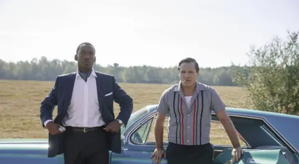Obsada filmu Green Book: Mahershala Ali w eleganckim garniturze i Viggo Mortensen w koszuli z lat 60. stoją obok siebie przy samochodzie.