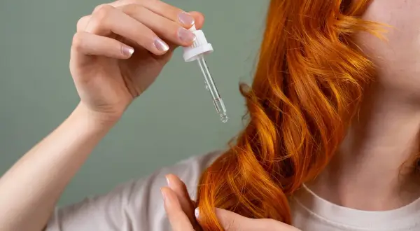 Kropla olejku rycynowego na włosy, aplikowana pipetką na lśniące, rude pasma.