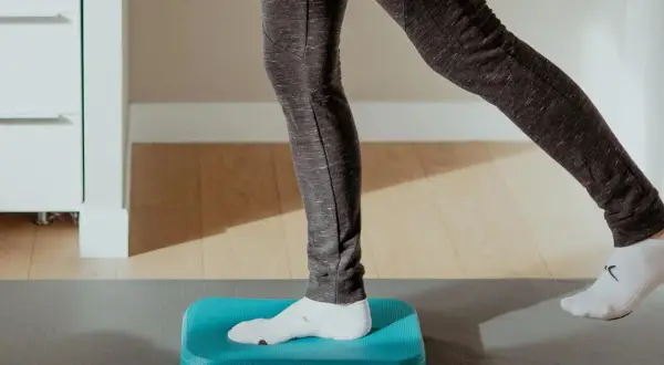 Exercice d'équilibre sur un coussin bleu pour améliorer la proprioception cheville.