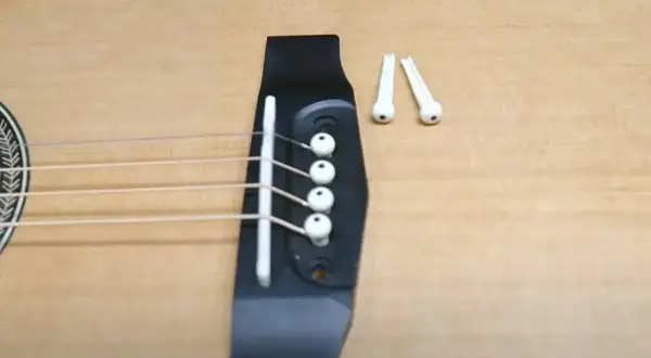 Jak zmienić struny w gitarze klasycznej? Widok na mostek gitary z naciągniętymi strunami i dwoma wyjętymi kołeczkami.