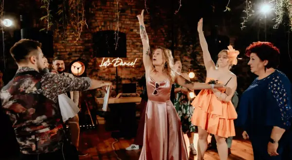 Oczepiny co to? Zabawa weselna w pełni! Panie w sukniach i panowie bawią się przy neonowym napisie "Let's Dance!".