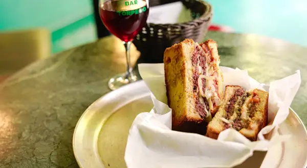 Un delicioso patty melt con carne jugosa y cebolla caramelizada, servido en pan tostado, junto a una copa de vino tinto.