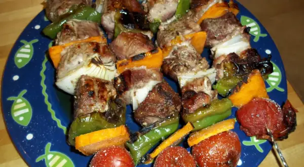 Brochetas de solomillo con pimientos verdes, cebolla y tomate, servidas en un plato azul con dibujos de peces.