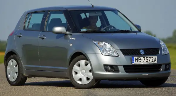 Szary Suzuki Swift na drodze. Kierowca w żółtej koszulce. Wiele osób chwali suzuki swift opinie o tym modelu są pozytywne.