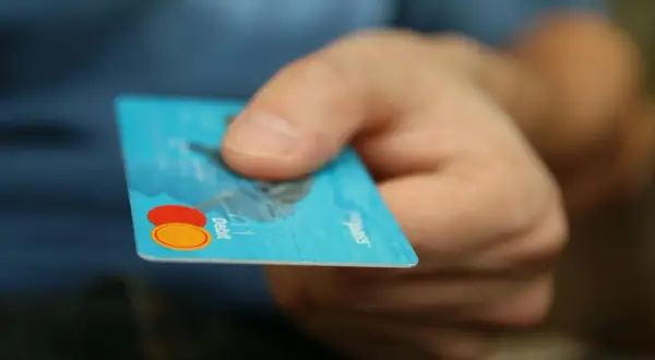 Dłoń trzyma niebieską kartę debetową z logo Mastercard.