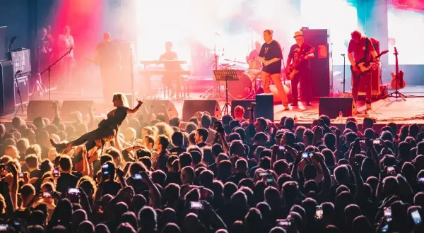 Energiczny koncert w klubie Stodoła Warszawa. Tłum szaleje, a na scenie gra zespół. Jedna z fanek jest niesiona przez publiczność.