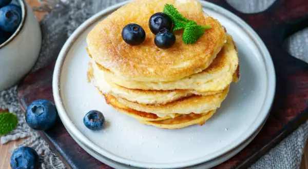 Ein Stapel fluffiger **Protein Pfannkuchen** mit Blaubeeren und Minze, bestäubt mit Puderzucker.