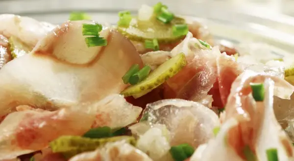 Ein deftiger Ochsenmaulsalat mit Gurken und Zwiebeln, garniert mit Schnittlauch. Perfekt für ein herzhaftes ochsenmaulsalat rezept.