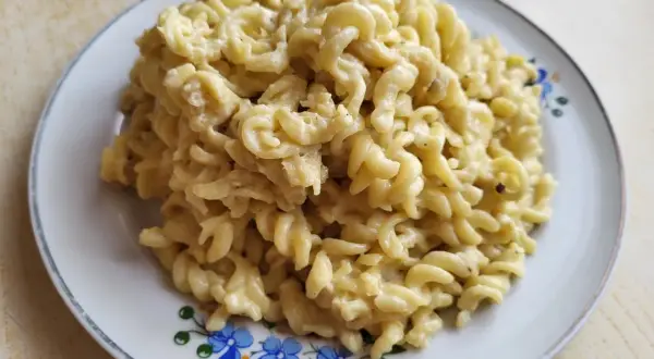 Pyszny makaron fusilli w kremowym sosie pieczarkowym, podany na talerzu z niebieskimi kwiatami.