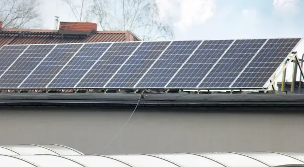 Panele fotowoltaiczne na dachu, gotowe do podgrzewania i produkcji energii. W tle budynki i drzewa.