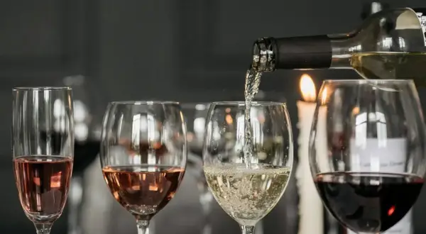 Degustacja wina w blasku świec. Nalewanie białego wina do kieliszka, obok różowe i czerwone wino.