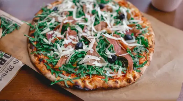 Pizza z rukolą, szynką parmeńską i oliwkami, posypana obficie startym parmezanem do pizzy.