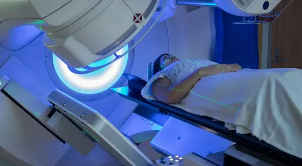 Frau liegt auf einem Tisch, während grüne Laserlinien auf sie gerichtet sind. Dies ist Teil der Bestrahlung bei Brustkrebs.