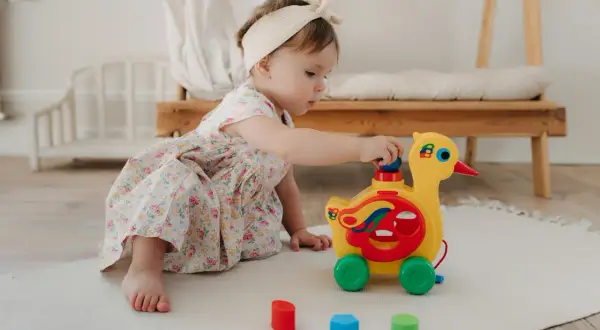 Mała dziewczynka w kwiecistej sukience bawi się żółtym pajacykiem zabawką na kółkach.