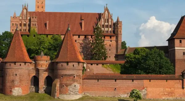 Potężny zamek w Malborku, wpisany na listę UNESCO w Polsce, z czerwonymi dachami i zielenią.