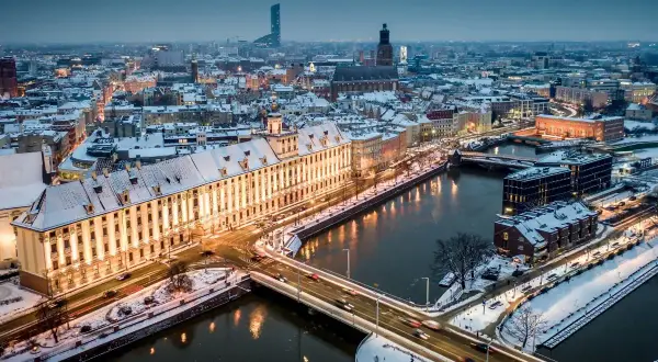 Zimowy Wrocław nocą. Ośnieżone dachy, rzeka i mosty tworzą magiczny widok. Warto odkrywać wrocławskie atrakcje zimą.