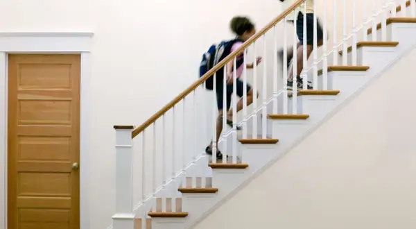 Two people with backpacks ascend a staircase with a new white stair railing and wooden handrail.